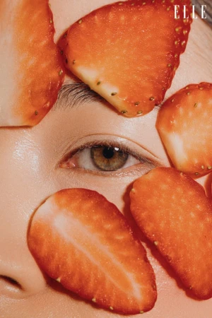 Close-up studio shot of a Caucasian woman's face partially covered with fresh strawberry slices, with the 'ELLE' logo visible.