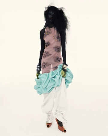 A dark-skinned fashion model poses in a halter top and white pants against a bright white backdrop in a studio fashion editorial.