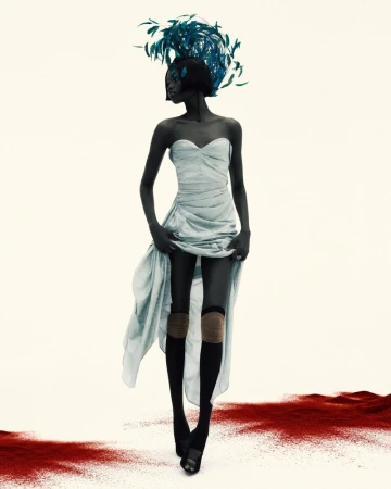 Fashion photo of an African American woman in a strapless dress and tall feathered headpiece, standing on a red dust surface.