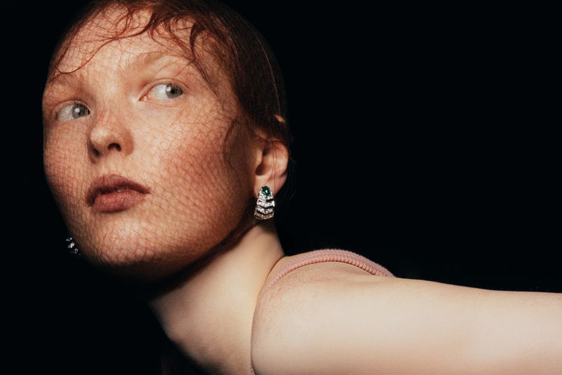 Close-up of a red-haired woman wearing jewelry and a net. Focus on the beauty and fashion elements in a dark studio setting.