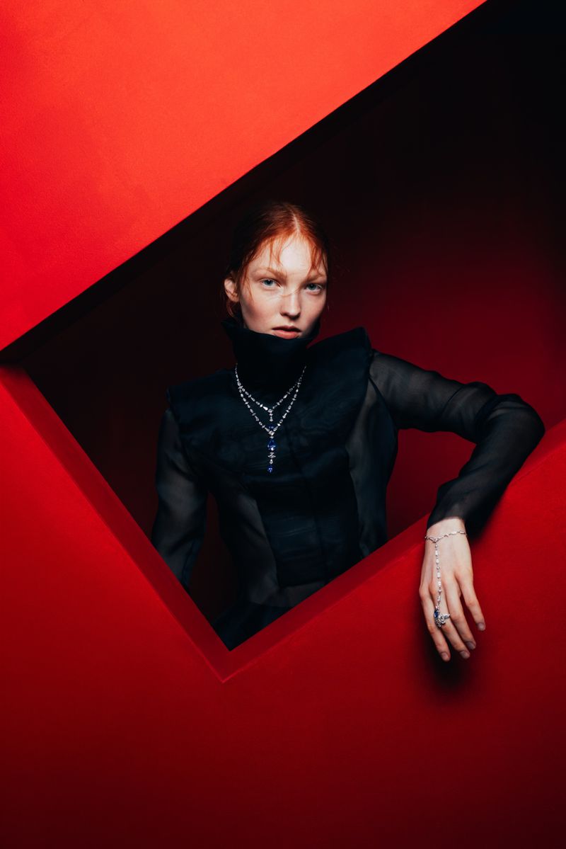Elegant portrait of a red-haired model in black clothing and jewelry, framed by a striking red geometric foreground.