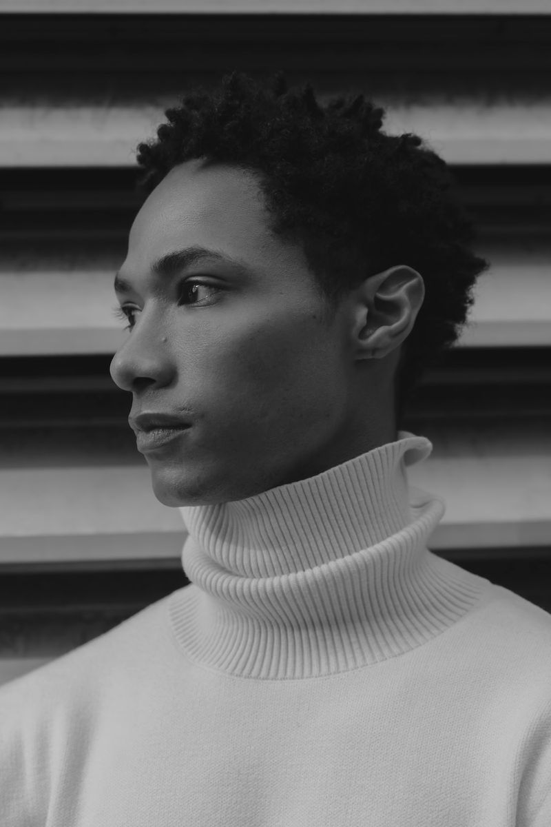 Black and white portrait of a model wearing a ribbed turtleneck sweater against a striped background