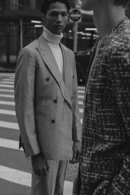 Monochrome shot of two men in suits standing on a city crosswalk, one facing forward and one partially cropped in a patterned suit.