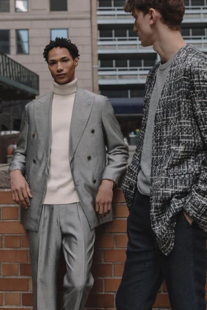 Two male models in tailored suits standing outside against a brick wall and city background for Kaltblut Magazine.