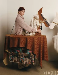 Male model wearing a brown beanie and textured cardigan inside a costume of a toy horse and table for Vogue China Men