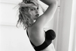 Monochrome portrait of a woman with tousled blonde hair wearing a dark bra against a plain background.