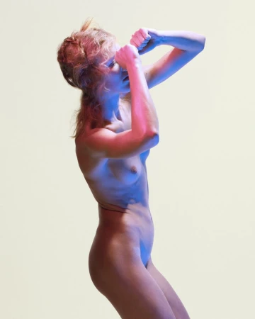 A side-profile shot of a person with auburn hair in an athletic pose, illuminated by contrasting blue and magenta studio lighting.