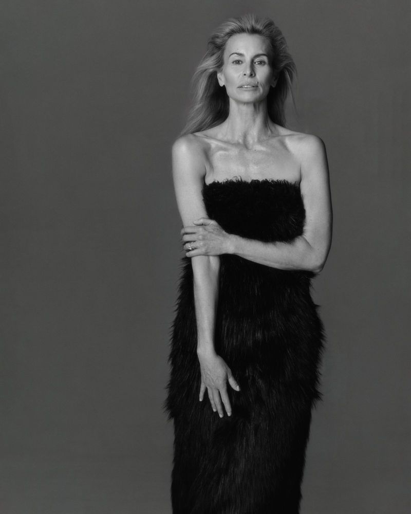 Elegant black and white portrait of a mature blonde woman in a feathered dress, posing against a plain backdrop with soft, diffused lighting.