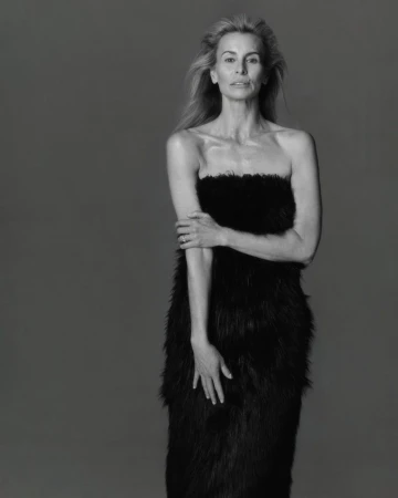 Elegant black and white portrait of a mature blonde woman in a feathered dress, posing against a plain backdrop with soft, diffused lighting.