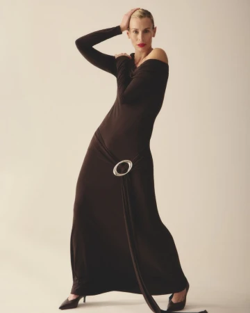 Model Niki Taylor wearing a long dark brown dress with a silver hip buckle against a seamless background