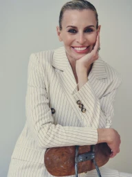 Model Niki Taylor smiling with hand to chin wearing a pinstripe suit for Harper's Bazaar Australia editorial.