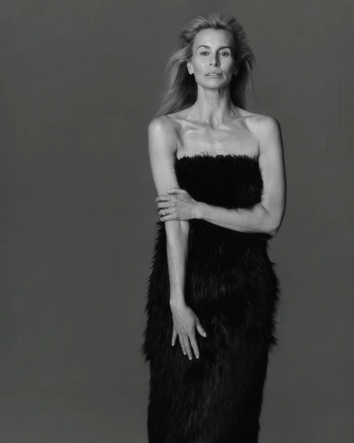 Model Niki Taylor wearing a textured black strapless dress against a solid grey studio background in a portrait shot.
