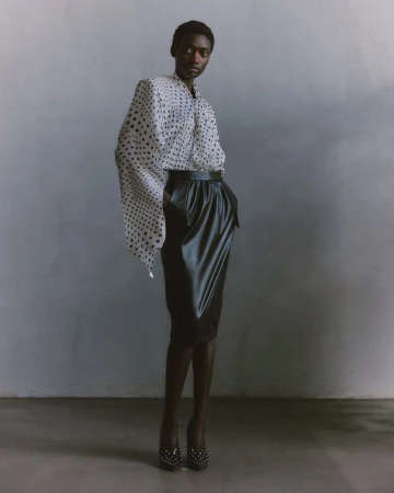 A striking full shot captures a Black female model in a polka dot blouse and black skirt, with a neutral background and studio lighting.