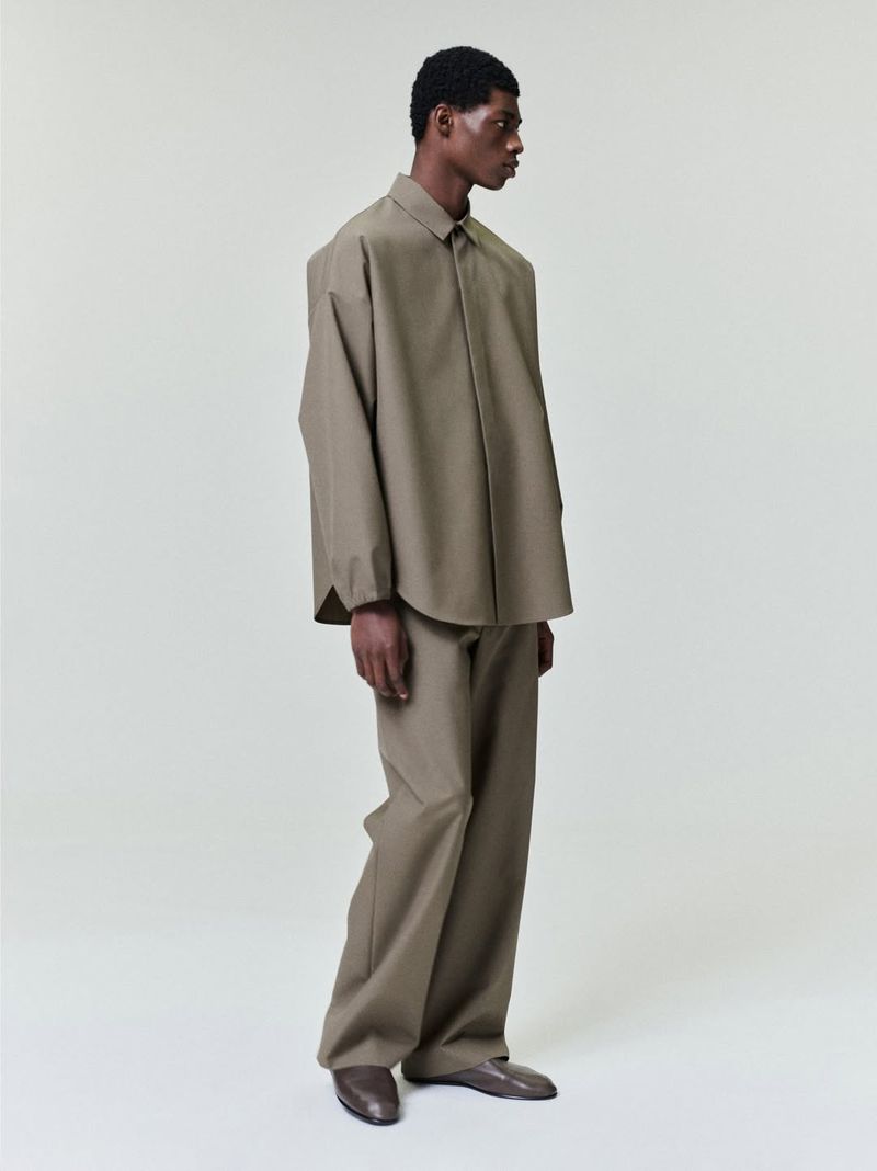 Fashion shot of an African-American man in a tan oversized shirt and pants, posing in a photo studio with soft lighting and modern style.