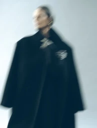 Motion blurred fashion portrait of a model wearing a dark coat against a plain light background