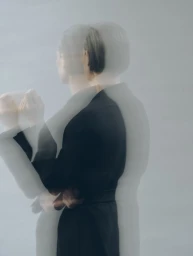 Multiple exposure portrait of a person in a black coat against a neutral grey studio background