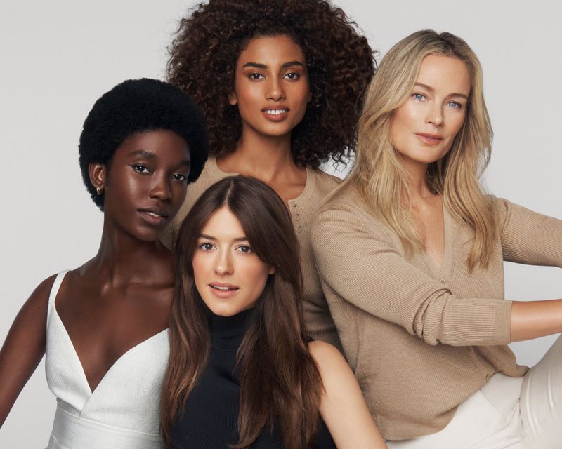 A group of four diverse women pose in a close-up studio shot, showcasing different skin tones and hair textures against a clean white background.