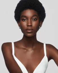 Portrait of a Black woman wearing a white top against a clean light grey background for Estee Lauder