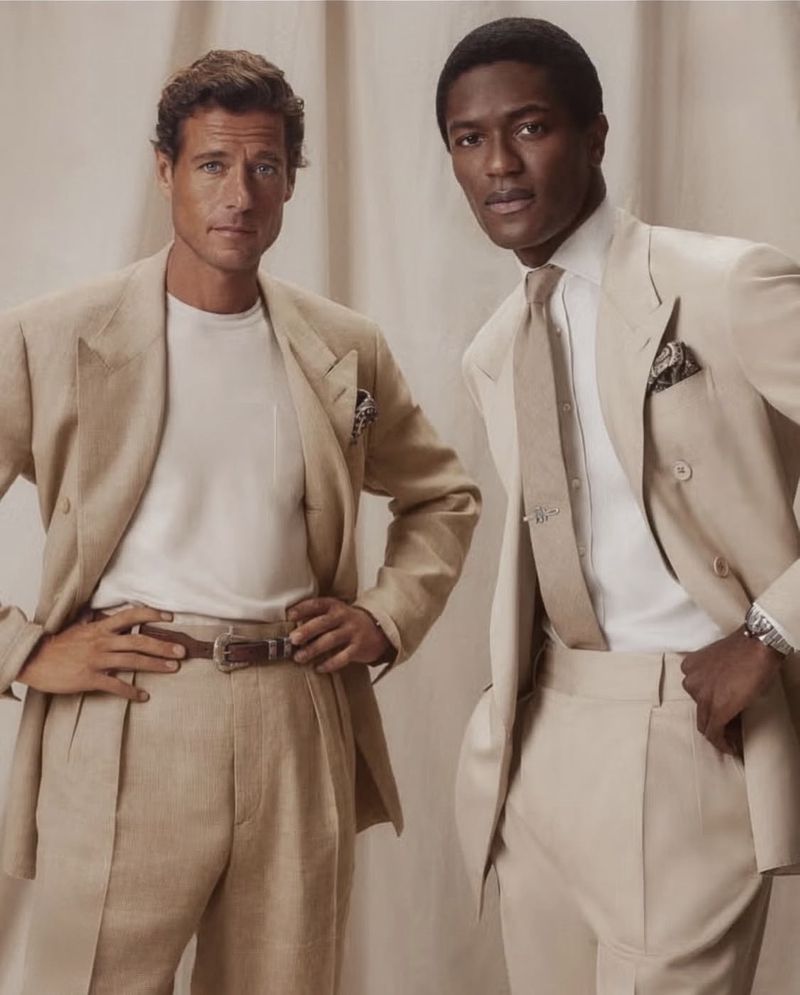 Two stylish men in tan suits pose indoors. One man is African American in a tie; the other is white wearing a t-shirt.