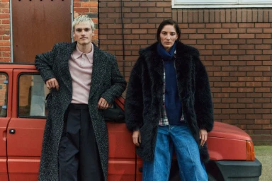 Two models posing outdoors against a brick wall next to a red car for The Observer Magazine UK fashion editorial.