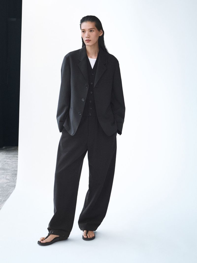 An Asian woman models a black blazer, vest, and wide-leg pants ensemble in a studio, with dark hair and neutral expression.