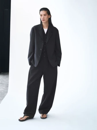 An Asian woman models a black blazer, vest, and wide-leg pants ensemble in a studio, with dark hair and neutral expression.