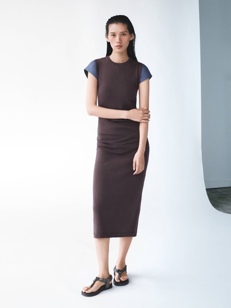 Full-length shot of a woman posing in a brown dress and sandals against a white background in a fashion setting. Studio lighting.