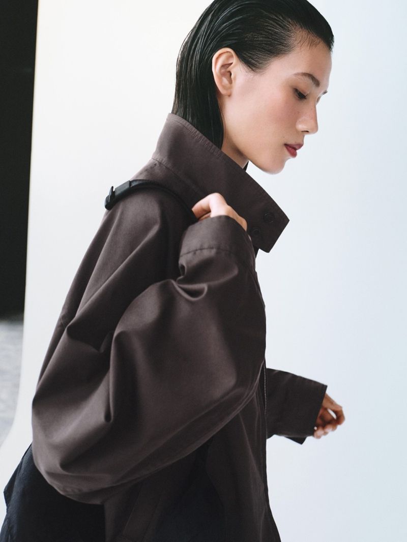 Portrait of an Asian woman wearing a brown coat against a light background in a studio, showcasing fashion and beauty.