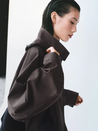 Portrait of an Asian woman wearing a brown coat against a light background in a studio, showcasing fashion and beauty.