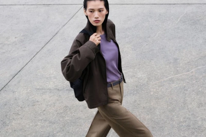 Model Jiayun Xie walking outdoors wearing a brown jacket over a purple top for the Uniqlo S/S 26 campaign photographed by Phil Engelhardt
