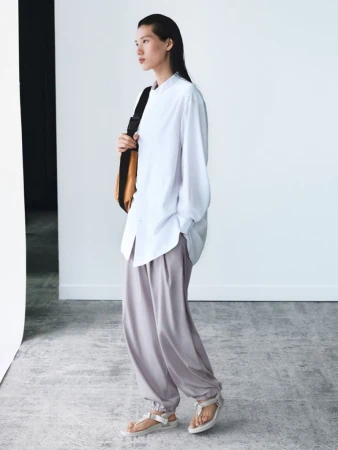 Model Jiayun Xie wearing a white long-sleeve shirt and grey trousers in a minimalist studio setting.