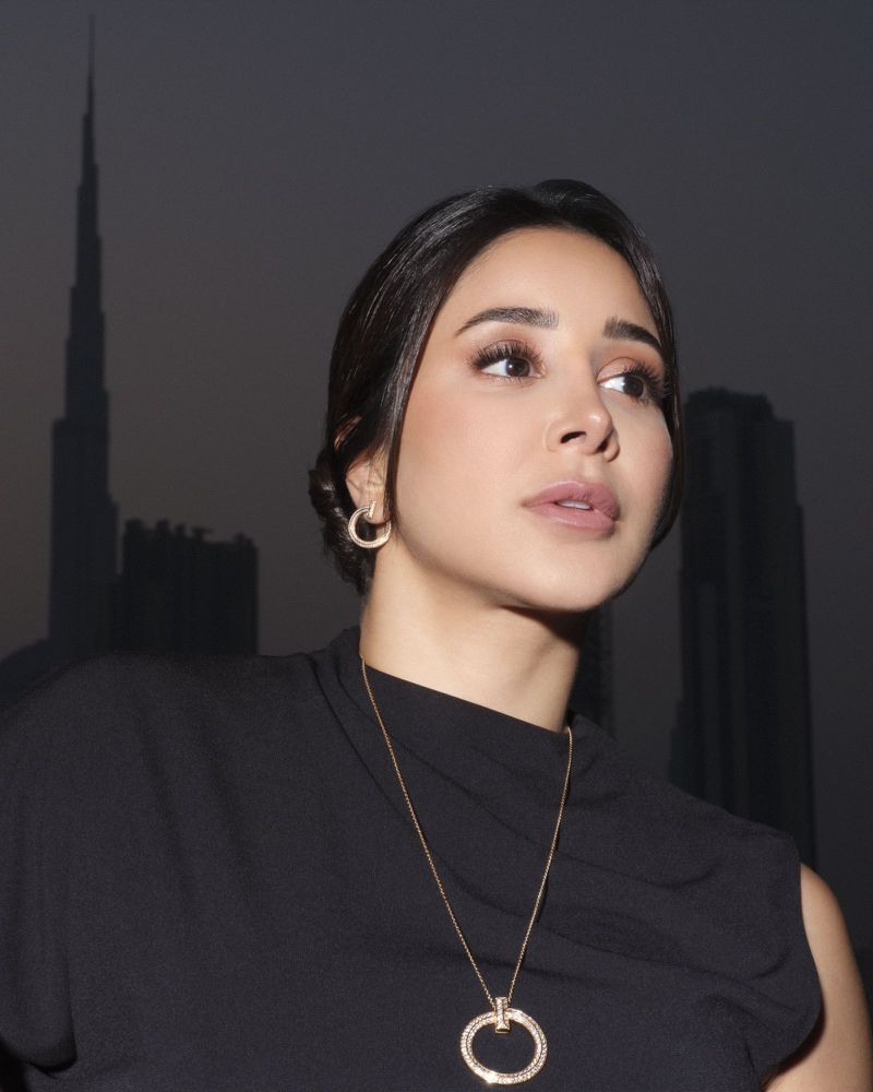 Portrait of a woman wearing jewelry with the Burj Khalifa skyscraper in the background. Focus on fashion and architecture.