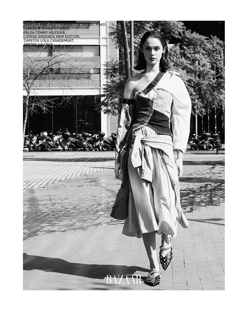Black and white editorial shot of a woman in draped and tied fashion, walking in an urban setting with motorbikes visible in the background.