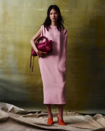 Model in pink dress holding magenta handbag against mottled green backdrop