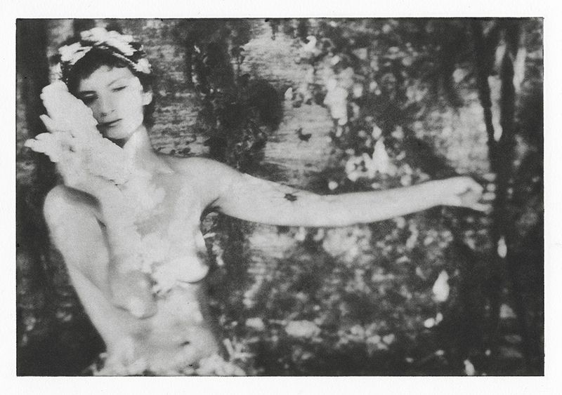 Monochrome portrait of a woman with floral crown holding a shell, artistic photography with dark, leafy background.