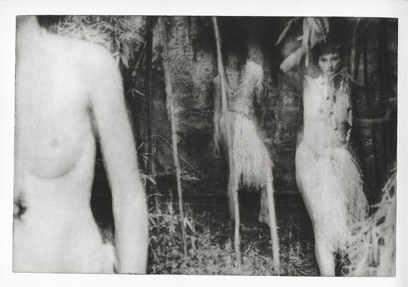 Monochrome photograph featuring a woman in a decorative outfit, standing in a jungle-like setting with foliage and branches.