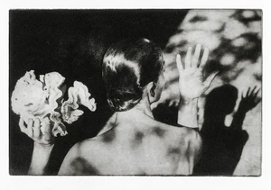 Monochrome editorial portrait of a person holding coral and raising a hand, casting shadows against a textured surface.