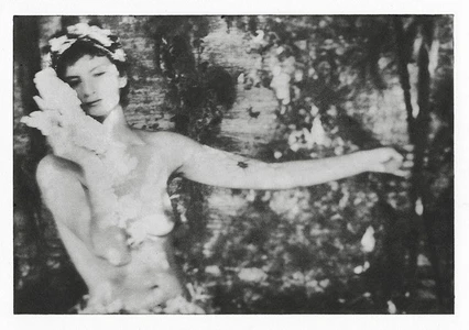 Black and white portrait of a woman wearing a floral headpiece holding a white object near her face, set against a textured woodland background.