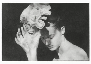 Monochrome fashion portrait of a woman holding a large white organic sculptural accessory above her head.
