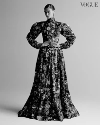 Model in a patterned long-sleeved gown with puffed shoulders standing against a seamless grey backdrop