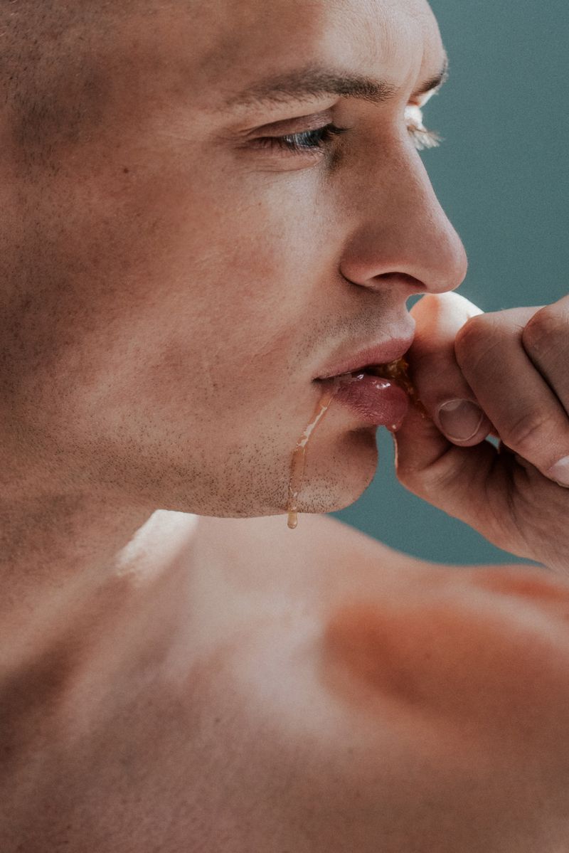 Close up of a man eating with golden liquid dripping from his lips against a plain background in a studio setting with side lighting.