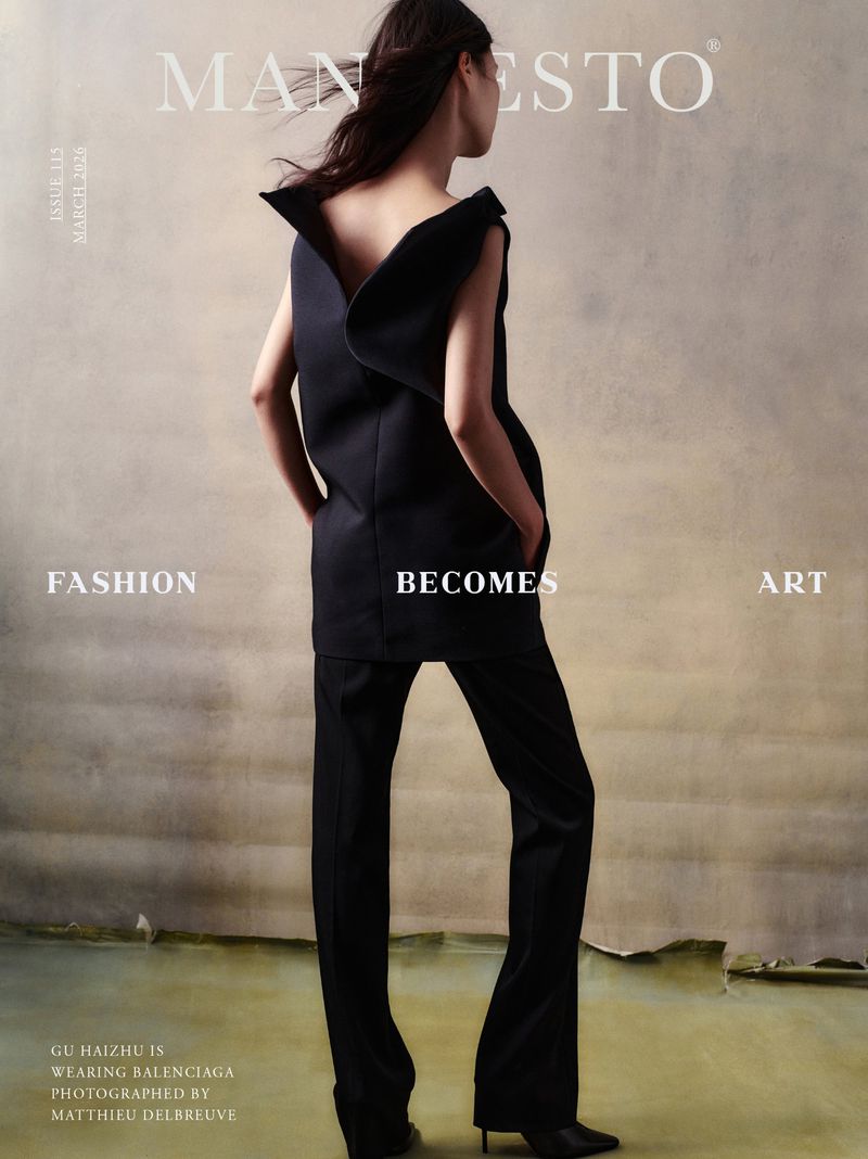 Fashion editorial: a woman in a black dress and pants stands in front of a mottled neutral backdrop for a Manifesto magazine cover.