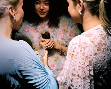 Three women chatting at an evening event, with an east asian woman in a colourful ruffled dress looking towards the camera.