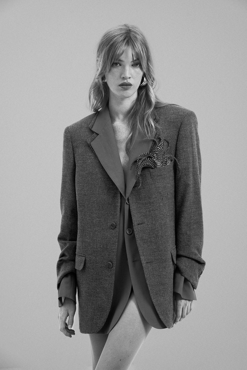 Black and white portrait of a woman in an oversized blazer, featuring a red under-layer, standing in front of a neutral backdrop.