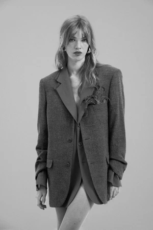 Black and white portrait of a woman in an oversized blazer, featuring a red under-layer, standing in front of a neutral backdrop.