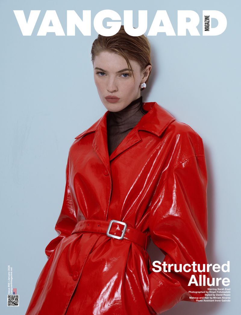 Fashion editorial cover shot featuring an adult woman in a shiny red coat and black turtleneck against a light blue background with magazine text.