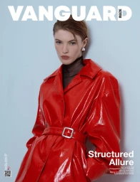 Model in a glossy red belted coat against a plain pale background for Vanguard Magazine
