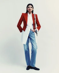 Model wearing a structured red blazer, white shirt, and blue jeans standing against a plain white studio background.