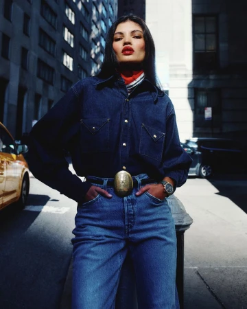 Model in denim shirt and jeans leaning on a street fixture against a city backdrop for Vogue Latin America