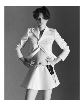 Monochrome fashion shot of a person in a white skirt suit, standing with hands on hips, showcasing a stylish and unique design.